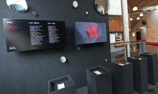 photograph of two screens with text and a 3D grid-based data visualisation in red on black
