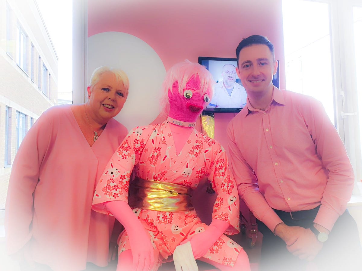 Two people dressed in pink surrounding a human-sized pink puppet