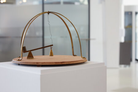 kinetic artwork of a circular wooden base and brass arches with a small brass seasaw with a weight