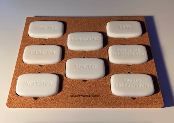 eight ivory coloured soap bars with different words engraved, arranged in a grid in a brown holder