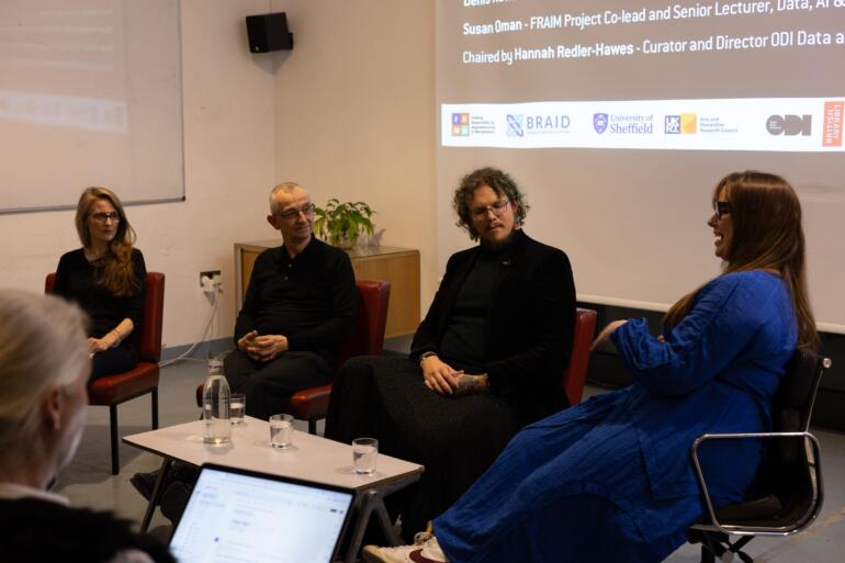 Four white people sitting around a low table in a discussion with a projection behind them